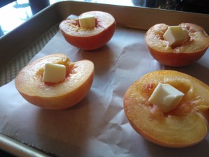 Halved peaches topped with butter, ready to be baked